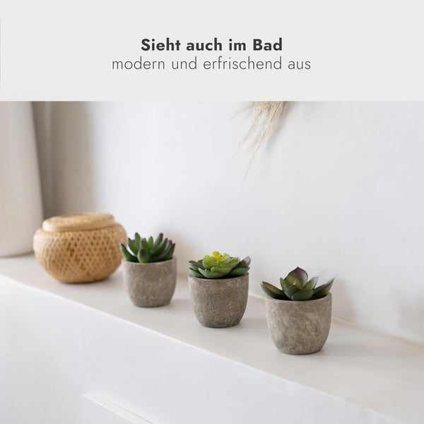 Drei kleine künstliche Sukkulenten in Steinoptik-Töpfen auf einer Ablage neben einem Korb, modern und erfrischend als Baddekoration.