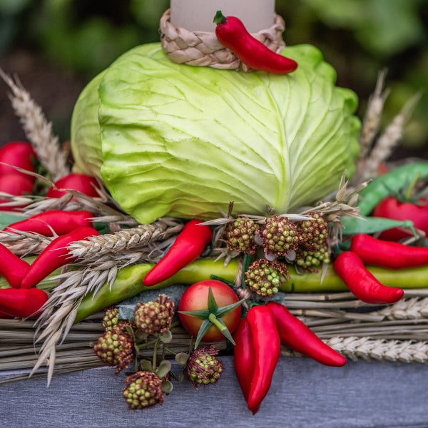 Dekoration mit Kohlkopf, Pfefferschoten, Weizenähren und Kerze