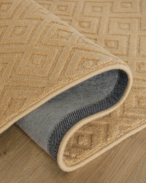 Beige Teppichläufer mit geometrischem Rautenmuster, Detail der Unterseite auf Holzboden.