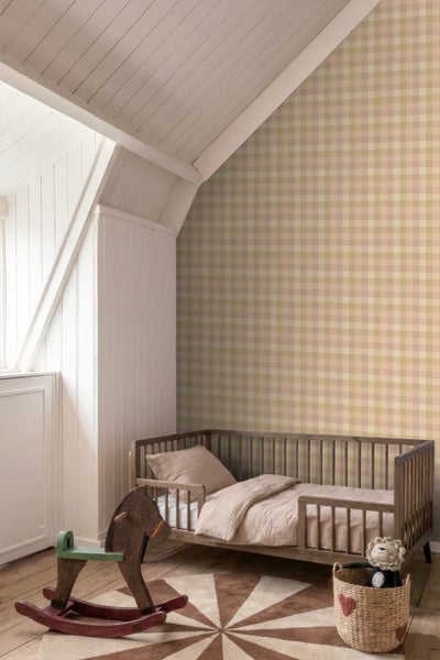 Kinderzimmer mit einer karierten Tapete, einem Holzbett und einem Schaukelpferd in einem hellen Dachgeschoss.