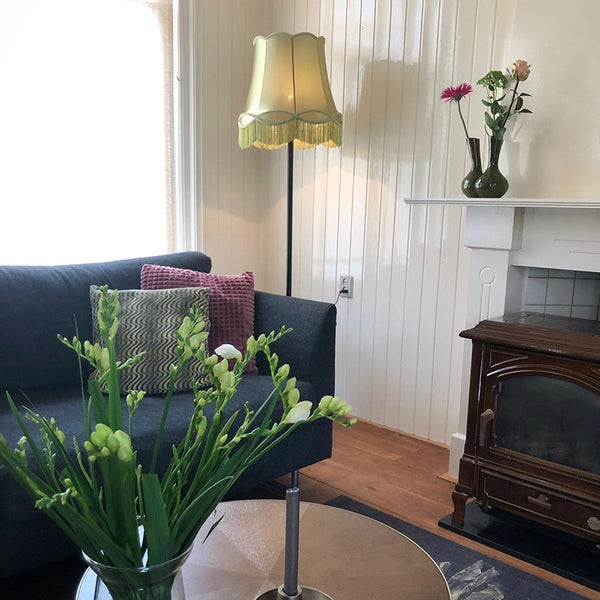 Gemütliches Wohnzimmer mit dunklem Sofa, Vintage-Stehlampe, weißen Wandpaneelen aus Holz und einem Kaminofen.
