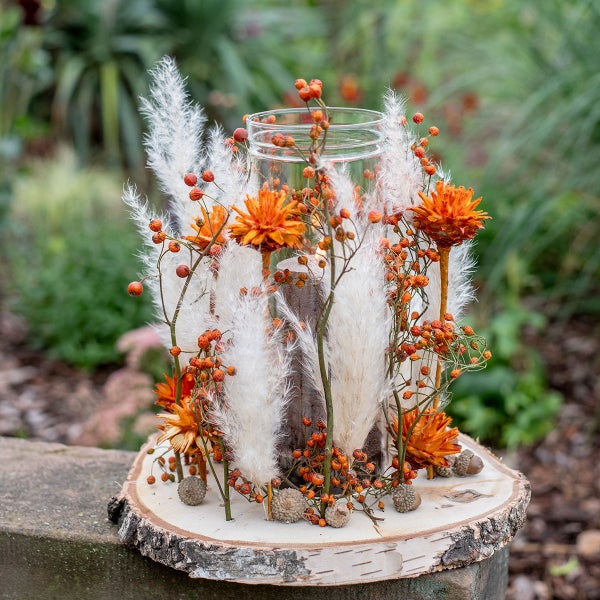 Dekorative Herbstdekoration mit Kerze, Trockenblumen und Beeren auf einem Baumstumpf
