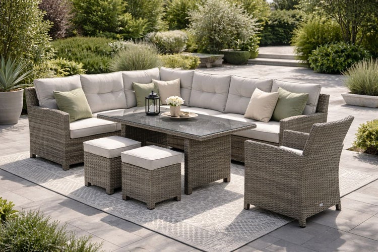 Garten-Lounge-Set aus Polyrattan-Geflecht mit großem Ecksofa, Sessel, zwei Hockern und Esstisch mit Glasplatte auf einer Terrasse im Garten.