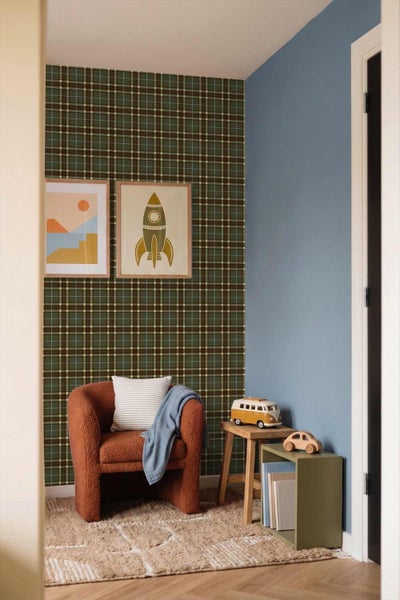 Gemütliche Zimmerecke mit dunkelgrün karierter Tapete, zwei Wandbildern, einem Sessel, Holzhocker mit Spielzeugbus und kleinem Regal.