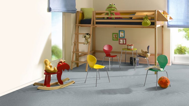 Ein helles Kinderzimmer mit hellblauem Teppichboden, einem Hochbett aus Holz, bunten Stühlen und verschiedenen Spielsachen.