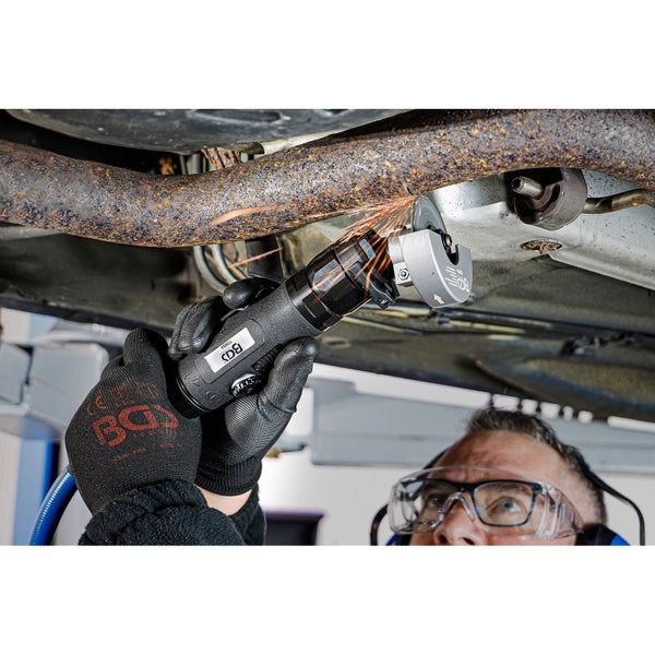 Ein Mann schneidet mit einem Druckluft-Rohrtrenner ein Auspuffrohr ab, wobei Funken entstehen