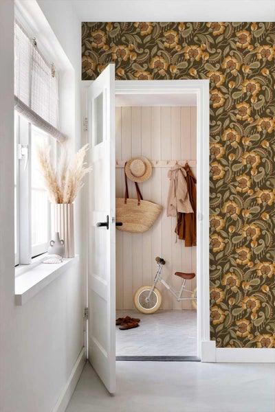 Heller Flur mit floral gemusterter Tapete neben einer weißen Tür, Blick in einen Raum mit Holzpaneelen und Kinderlaufrad.