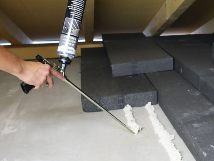 Anwendung von Dämmstoffkleber mit einer Schaumpistole auf einem Boden zur Befestigung von grauen Dämmplatten im Dachgeschoss.