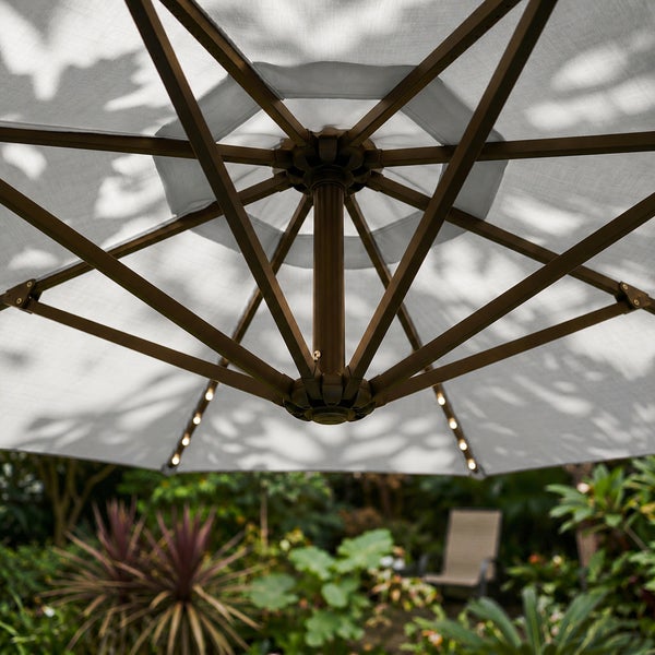 Unteransicht eines Sonnenschirms mit integrierter LED-Beleuchtung an den Streben in einem hellen Garten.