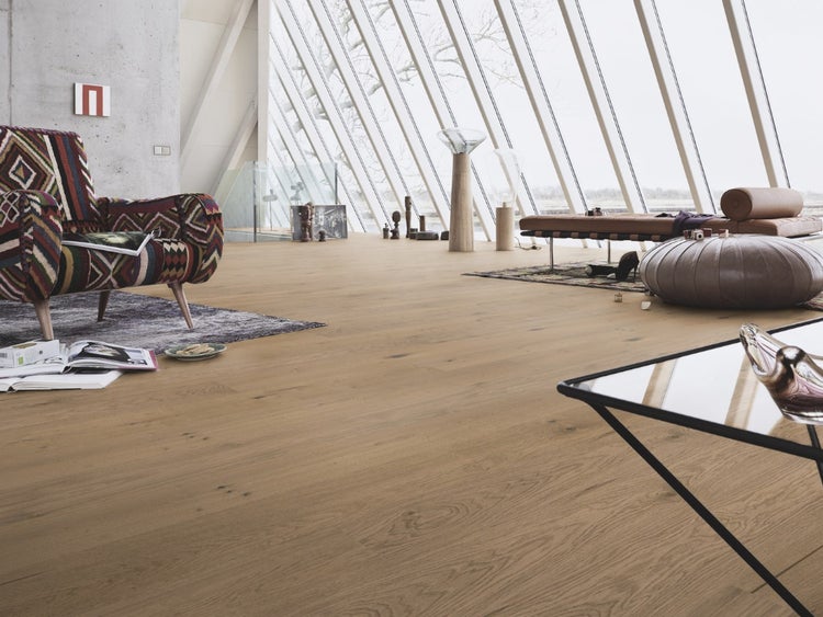 Heller Parkettboden in einem modernen Wohnzimmer mit großen schrägen Fenstern, einem gemusterten Sessel und einer Lederliege.