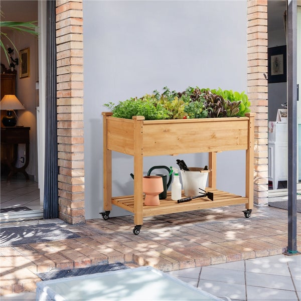 Hochbeet aus Holz mit Pflanzen, Gießkanne und Gartengeräten auf der Terrasse