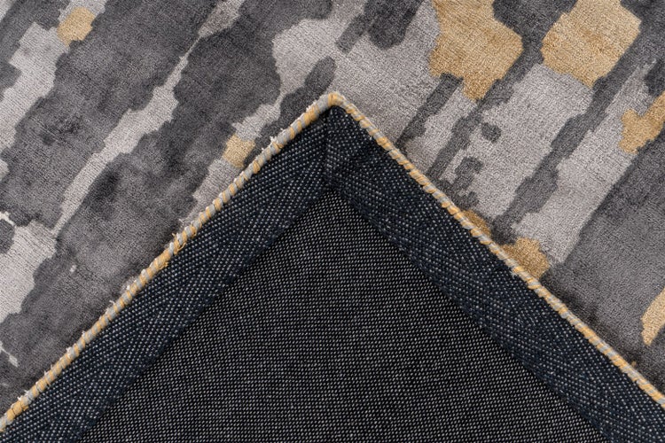 Nahaufnahme eines Teppichs mit abstraktem Muster und geketteltem Rand, die Oberseite und die strukturierte Rückseite zeigt.