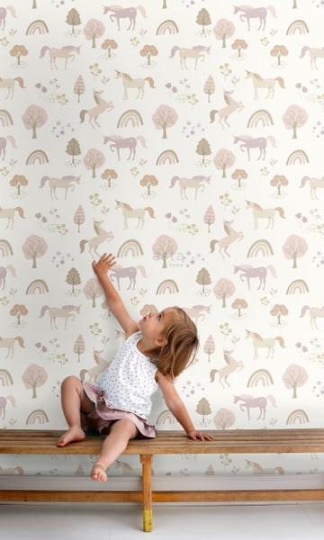 Mädchen sitzt vor einer Wand mit Einhorn Tapete.