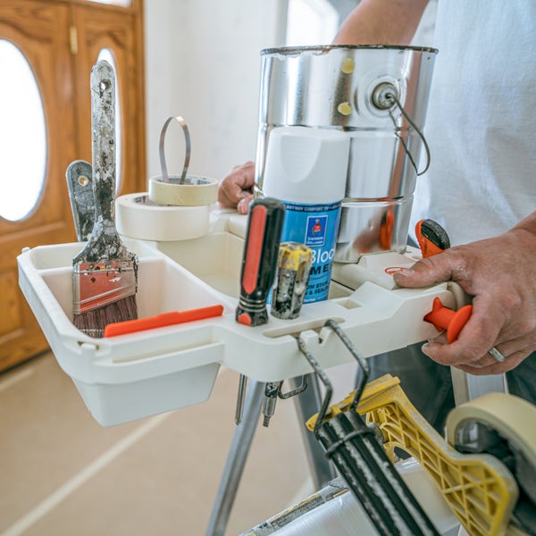 Werkzeugablage an einer Leiter befestigt, bestückt mit Farbdosen, Pinseln und Malwerkzeug bei einer organisierten Innenrenovierung.