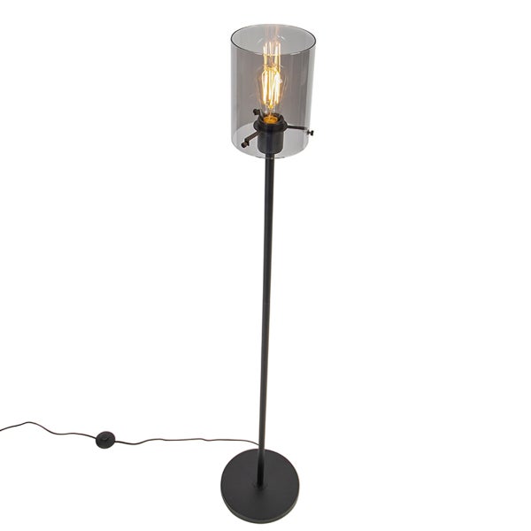 Stehlampe aus schwarzem Metall mit zylindrischem Schirm aus Rauchglas, Filament-Leuchtmittel und Fußschalter.