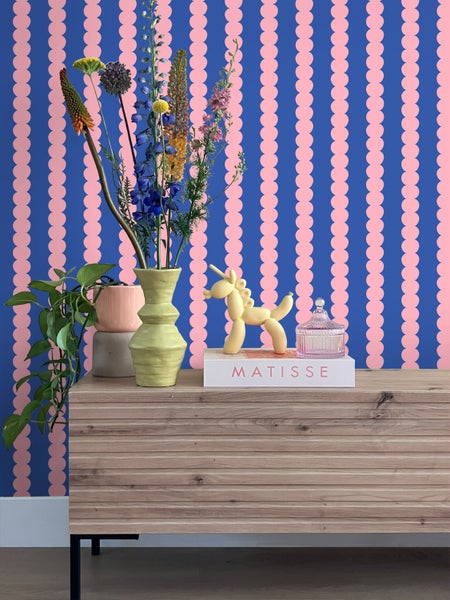 Dekoratives Arrangement auf einer Kommode mit gemusterten Tapeten im Hintergrund