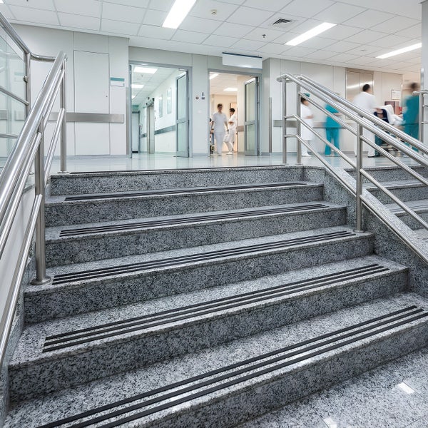 Steintreppe mit Edelstahlgeländer in einem Krankenhausflur mit medizinischem Personal im Hintergrund