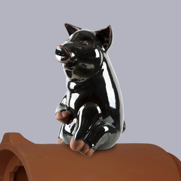 Firstschmuck Schwein aus schwarzer glasierter Keramik, sitzend auf einem braunen Firstziegel.