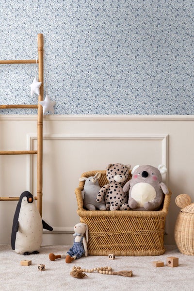 Kinderzimmer mit blau gemusterter Blumentapete, Wandleisten, Bambusleiter, Korbstuhl und Stofftieren.