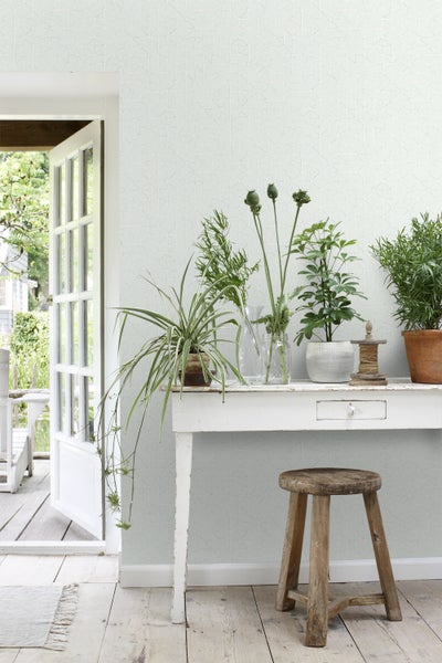 Helles Zimmer mit gemusterter Tapete, dekoriert mit Pflanzen auf einem Tisch und einem Hocker