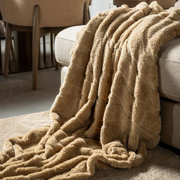 Beige Kuscheldecke drapiert auf einem Sofa.