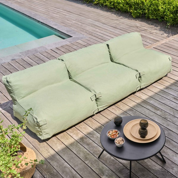 Hellgrünes dreisitziges Outdoor-Sitzsack-Sofa auf einer hellen Holzterrasse neben einem Pool mit schwarzem Beistelltisch.