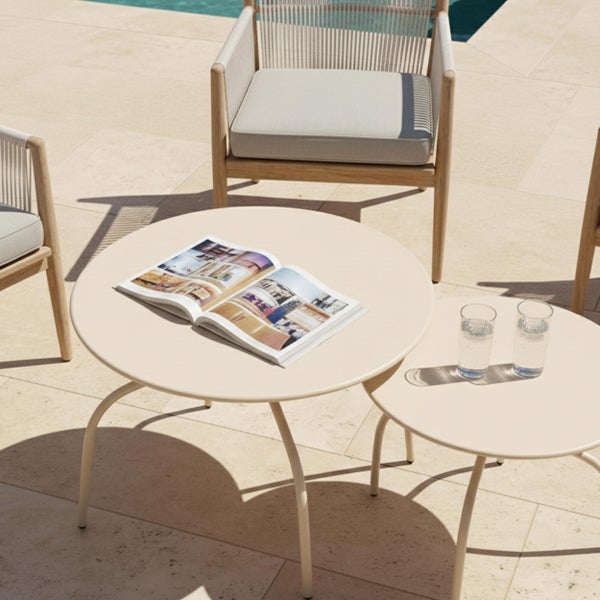 Zwei beige runde Beistelltische aus Metall auf einer Terrasse mit modernen Gartenstühlen aus Holz.