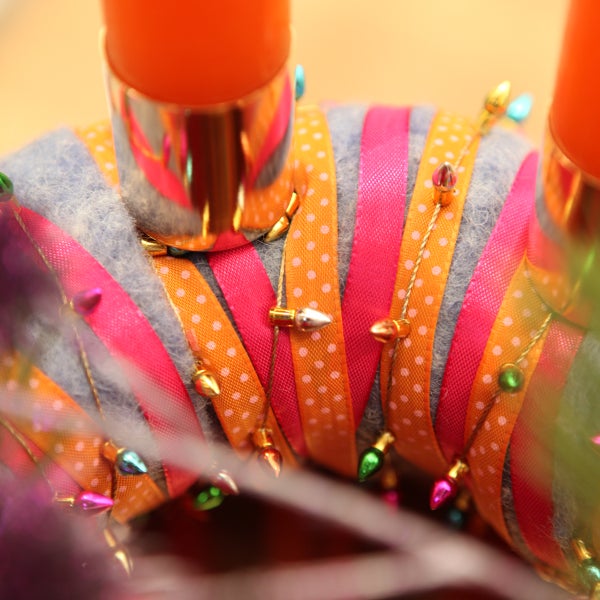 Detailansicht eines Adventskranzes mit Kerzenhaltern, Bändern und kleinen Lichtern