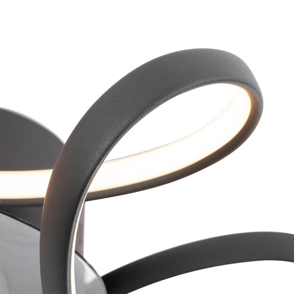 Detailansicht einer modernen LED-Leuchte mit geschwungenen, schwarzen Elementen und warmweißem Licht.