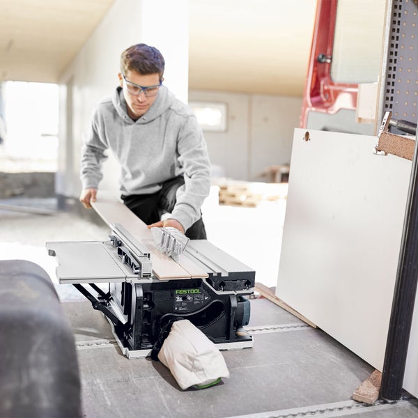 Ein Handwerker mit Schutzbrille schneidet eine Holzdiele mit einer Festool Tischkreissäge in einem Transporter zu.