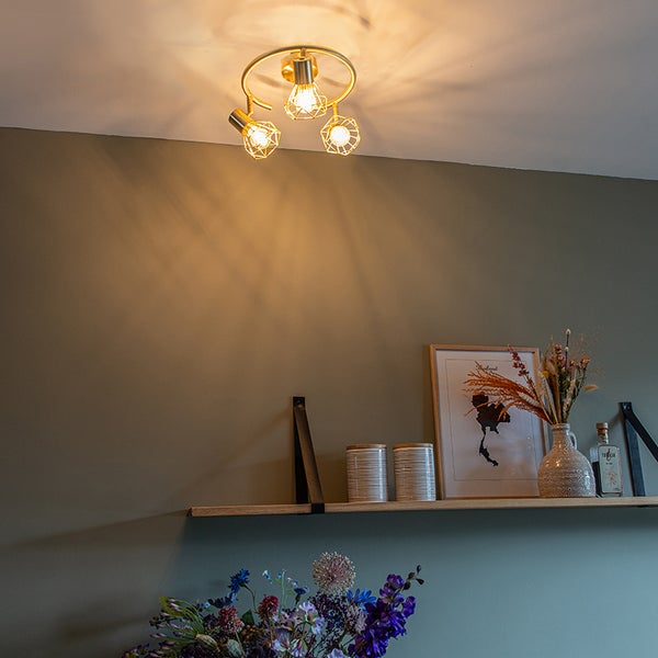 Goldfarbene Deckenleuchte mit drei Leuchten in einem Wohnraum.