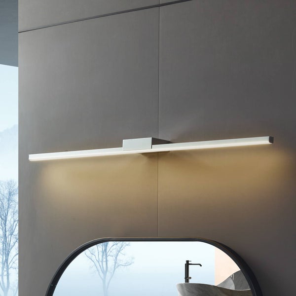 Moderne LED-Badwandleuchte in Chrom-Optik, montiert über einem Badezimmerspiegel an einer dunklen Wand. Schlankes, minimalistisches Design.