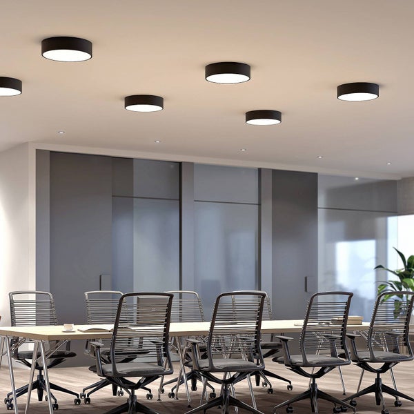 Moderner Konferenzraum mit runden schwarzen LED-Deckenleuchten, großem Besprechungstisch und Bürostühlen mit Netzbespannung.