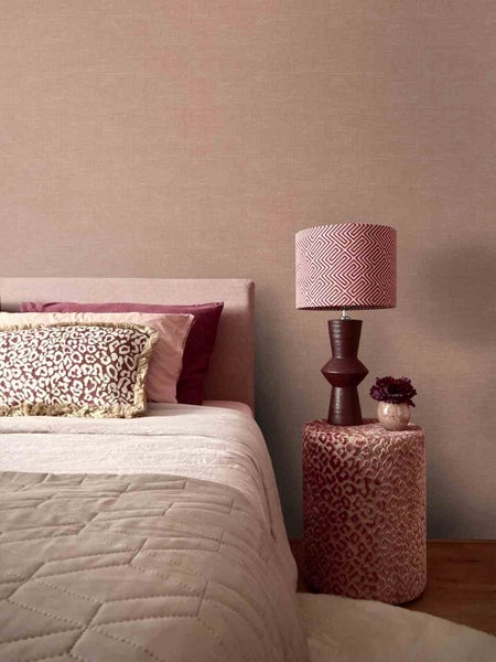 Strukturierte Tapete in einem Schlafzimmer mit Bett, Kissen im Leopardmuster, Tischlampe mit geometrischem Muster und einem Hocker.