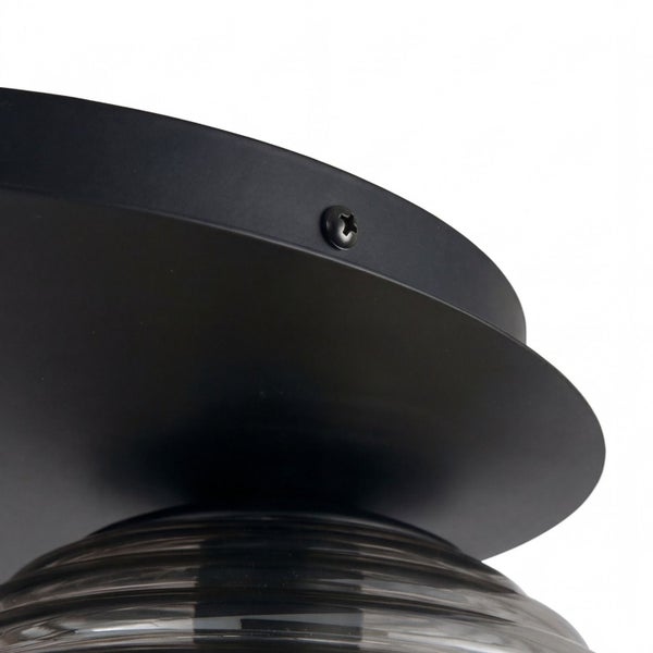 Detailansicht einer schwarzen Lampenhalterung aus Metall mit einer Schraube und einem gerippten Glasschirm.