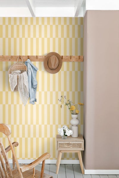 Vliestapete mit gelbem und weißem geometrischem Rechteckmuster in einem hellen Raum mit Holzmöbeln und Wandgarderobe.