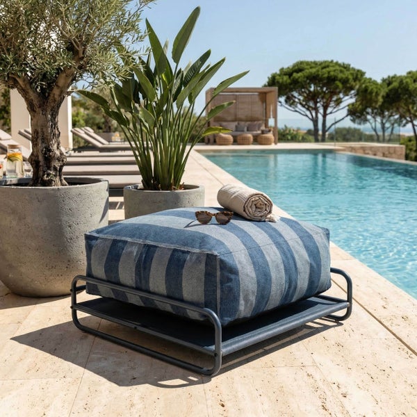 Gestreiftes Bodenkissen für den Außenbereich auf einem Metallgestell neben einem Pool mit Pflanzen in Töpfen.