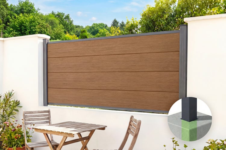 Moderner Sichtschutzzaun in brauner Holzoptik mit anthrazitfarbenem Aluminiumrahmen, montiert auf einer weißen Mauer im Garten mit Sitzgruppe.