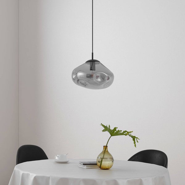 Moderne Pendelleuchte mit unregelmäßig geformtem rauchgrauem Glasschirm über einem runden Esstisch in einem hellen Raum.