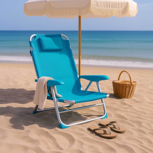 Helle Strandszene mit blauem Klapp-Liegestuhl aus Aluminium, cremefarbenem Sonnenschirm mit Fransen, Flechtkorb und Flip-Flops auf dem Sand am Meer.