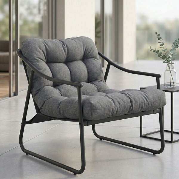 Moderner Loungesessel mit dunklem Metallgestell und dickem grauem Steppkissen auf einer Terrasse neben einem Beistelltisch.