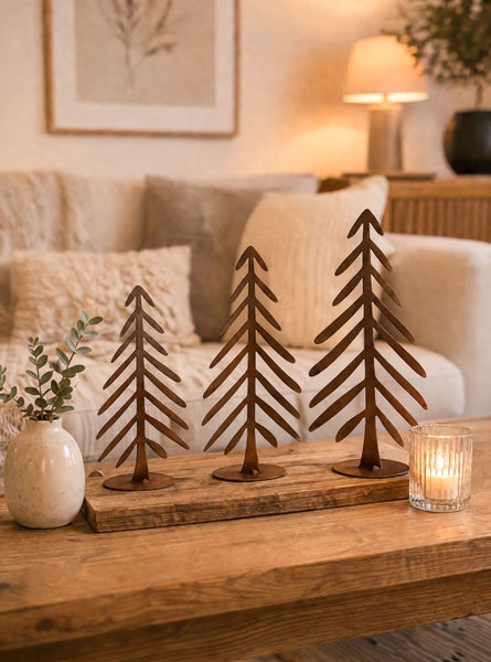 Drei stilisierte Tannenbäume aus Metall auf einem Holzbrett als weihnachtliche Tischdekoration in einem gemütlichen Wohnzimmer.