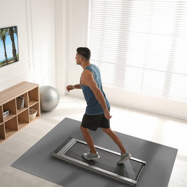 Mann auf kompaktem Laufband in hellem Fitnessraum mit Regal, Fenster und Gymnastikball auf Schutzmatte.