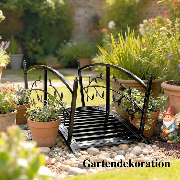 Dekorative Gartenbrücke aus Metall mit Blattornamenten in einer hellen Gartenlandschaft mit Tontöpfen und Pflanzen.