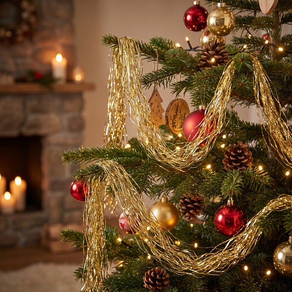 Weihnachtsbaum geschmückt mit Kugeln und Lametta vor einem gemütlichen Kamin im Wohnzimmer.