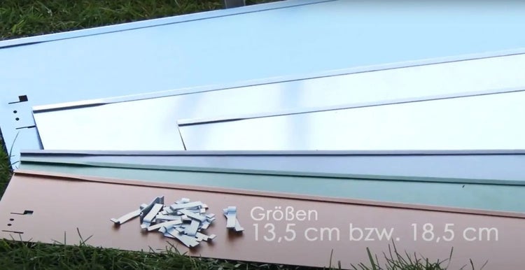 Mehrfarbige Metallplatten und Montagezubehör mit Größenangabe 13,5 Zentimeter beziehungsweise 18,5 Zentimeter.