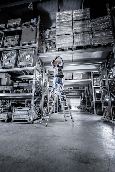 Mann auf einer Stufenleiter in einem Lagerhaus mit Regalen