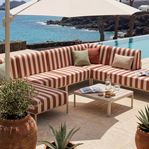 Gestreifte Ecklounge mit passendem Hocker, quadratischem Beistelltisch und großem Sonnenschirm auf einer Terrasse am Pool mit Meerblick.