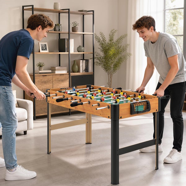 Zwei Personen spielen Tischfußball an einem Kickertisch in Holzoptik in einem hellen Wohnzimmer.