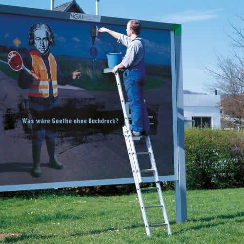 Ein Handwerker steht auf einer Aluminium-Mehrzweckleiter und beklebt eine große Werbetafel im Freien.
